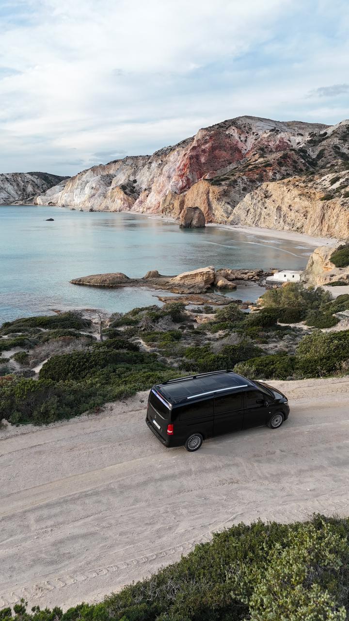 Elysium Transfer Milos vehicle on a coastal road above a bay on Milos